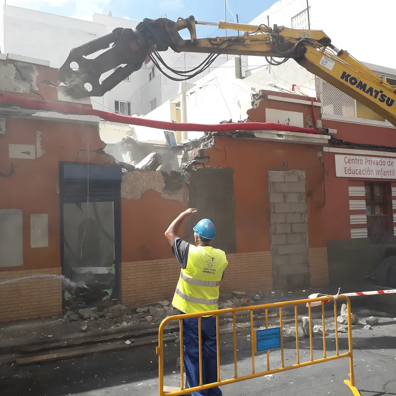 Pinza de demolición derribando una fachada en casco urbano con operario de seguridad